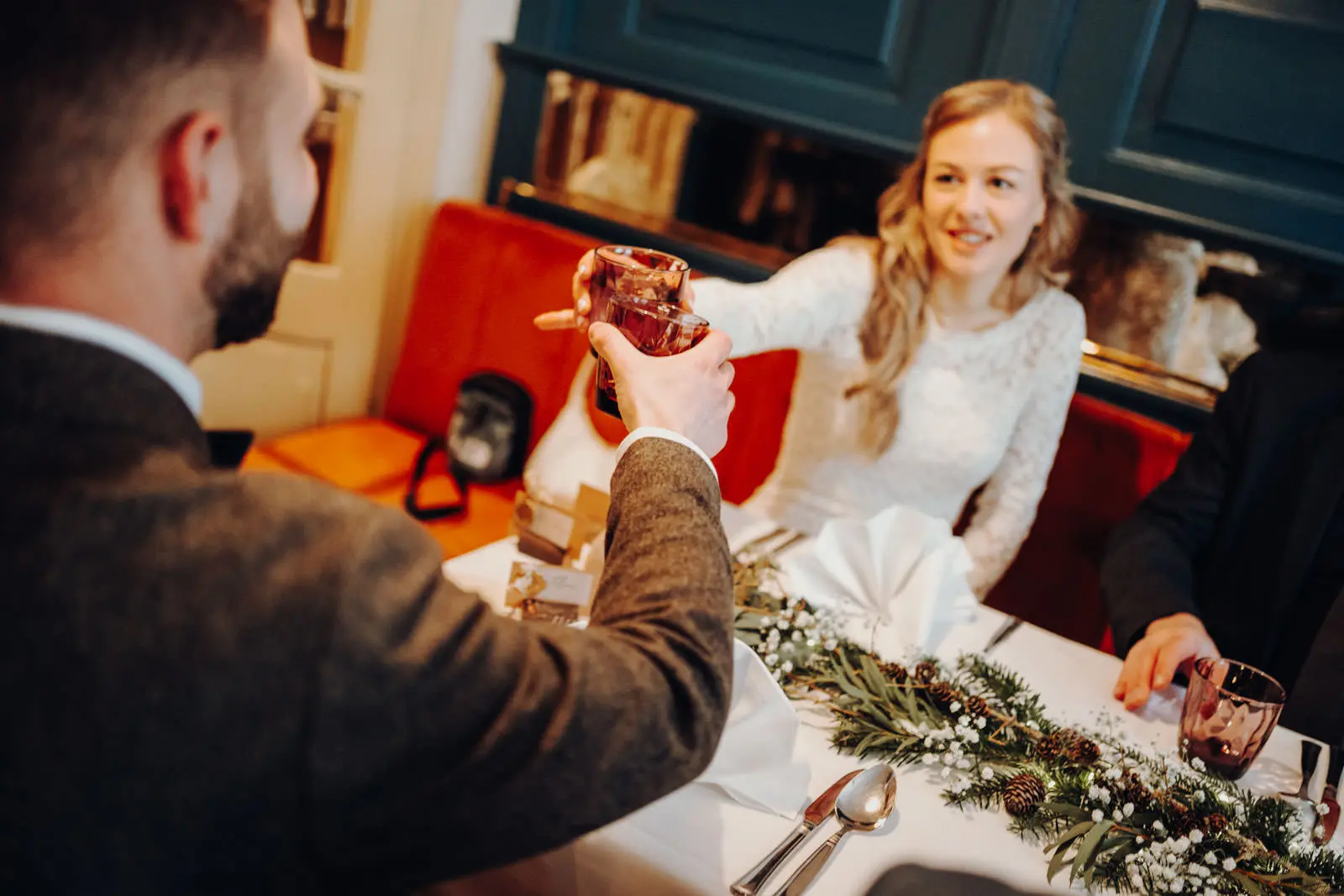 Brautpaar stoesst an beim Hochzeitsempfang Braut und Braeutigam stossen mit Glaesern am festlich gedeckten Tisch beim Hochzeitsempfang an, Tannenzweig-Tischdeko im Vordergrund.