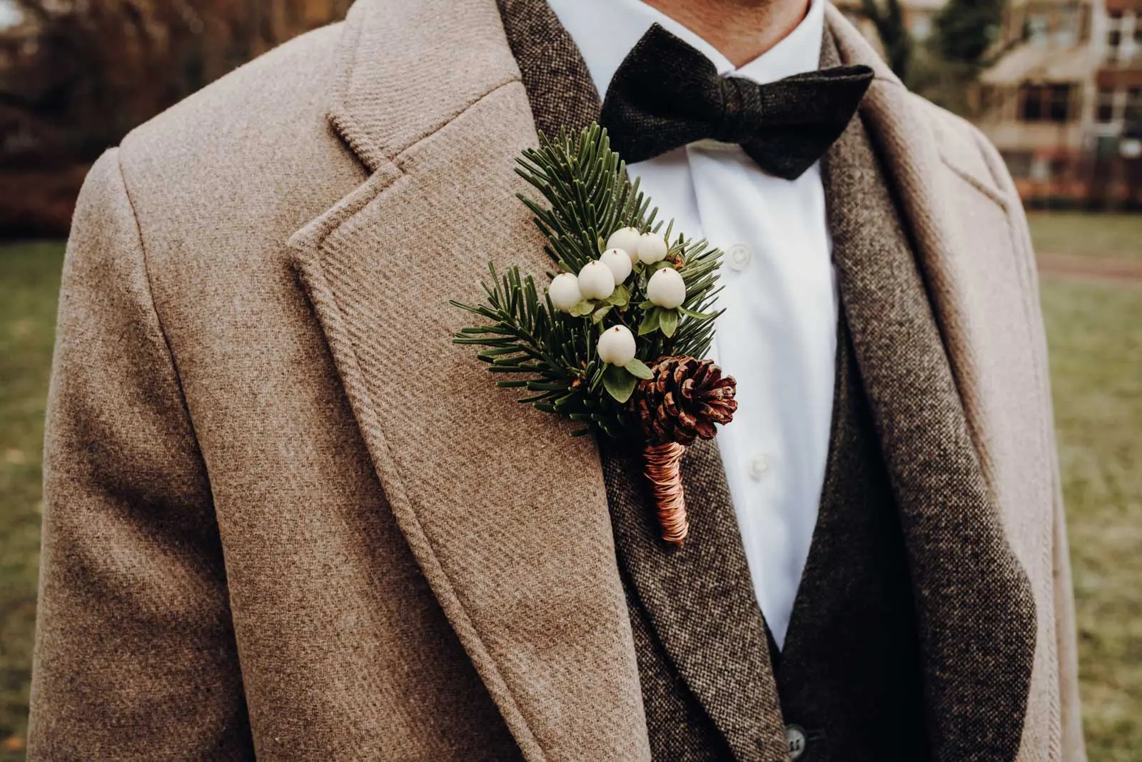 Boutonniere Braeutigam – Tannenzweig und weisse Beeren Nahaufnahme der Boutonniere am Revers des Braeutigams mit Tannenzweig, weissen Beeren und Tannenzapfen.