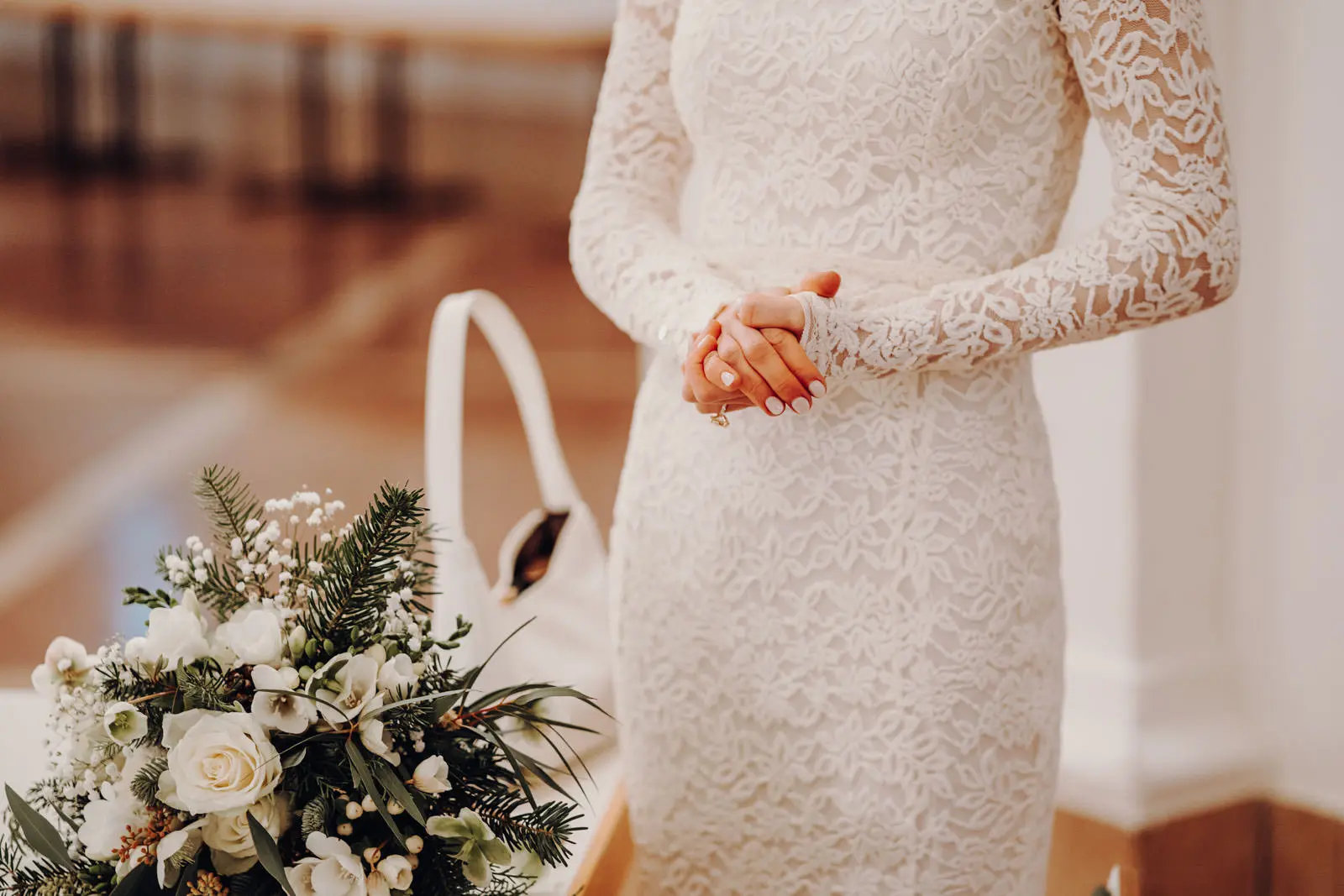 Braut mit Winterstrauss – Wartemoment vor der Trauung Braut im Spitzenkleid haelt die Haende gefaltet, neben ihr ein winterlicher Strauss mit weissen Rosen und Tannenzweigen.