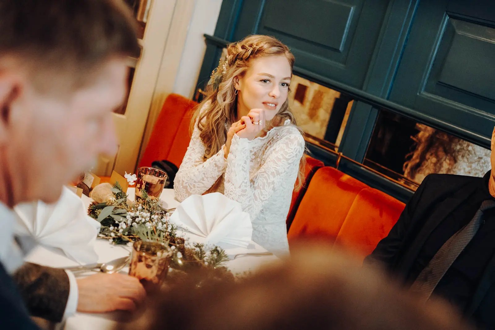 Braut beim Hochzeitsempfang im Coffe Baum Leipzig Braut im Spitzenkleid sitzt laechelnd am festlich gedeckten Tisch beim Hochzeitsempfang, roter Samtpolstersessel im Hintergrund.