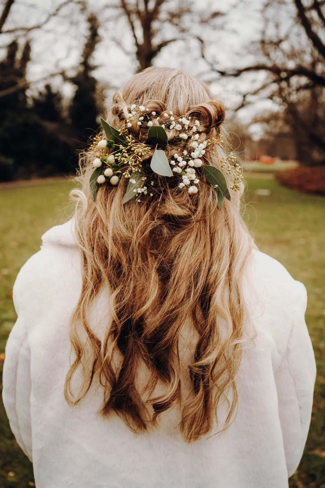 Haarschmuck der Braut – Blumen und Eukalyptus Rueckenaufnahme der Braut mit lockerem Hochsteckzopf, verziert mit weissen Beerenrispen, Schleierkraut und Eukalyptus.