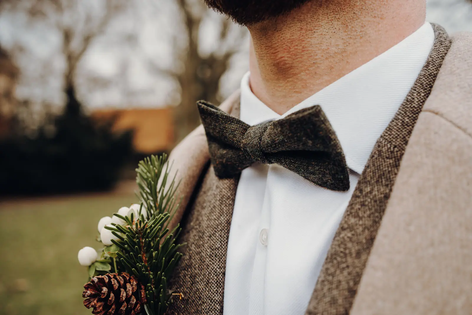 Tweed-Fliege und Boutonniere des Braeutigams Detailaufnahme der Tweed-Fliege am weissen Hemd des Braeutigams mit Boutonniere aus Tannenzweig und Tannenzapfen.