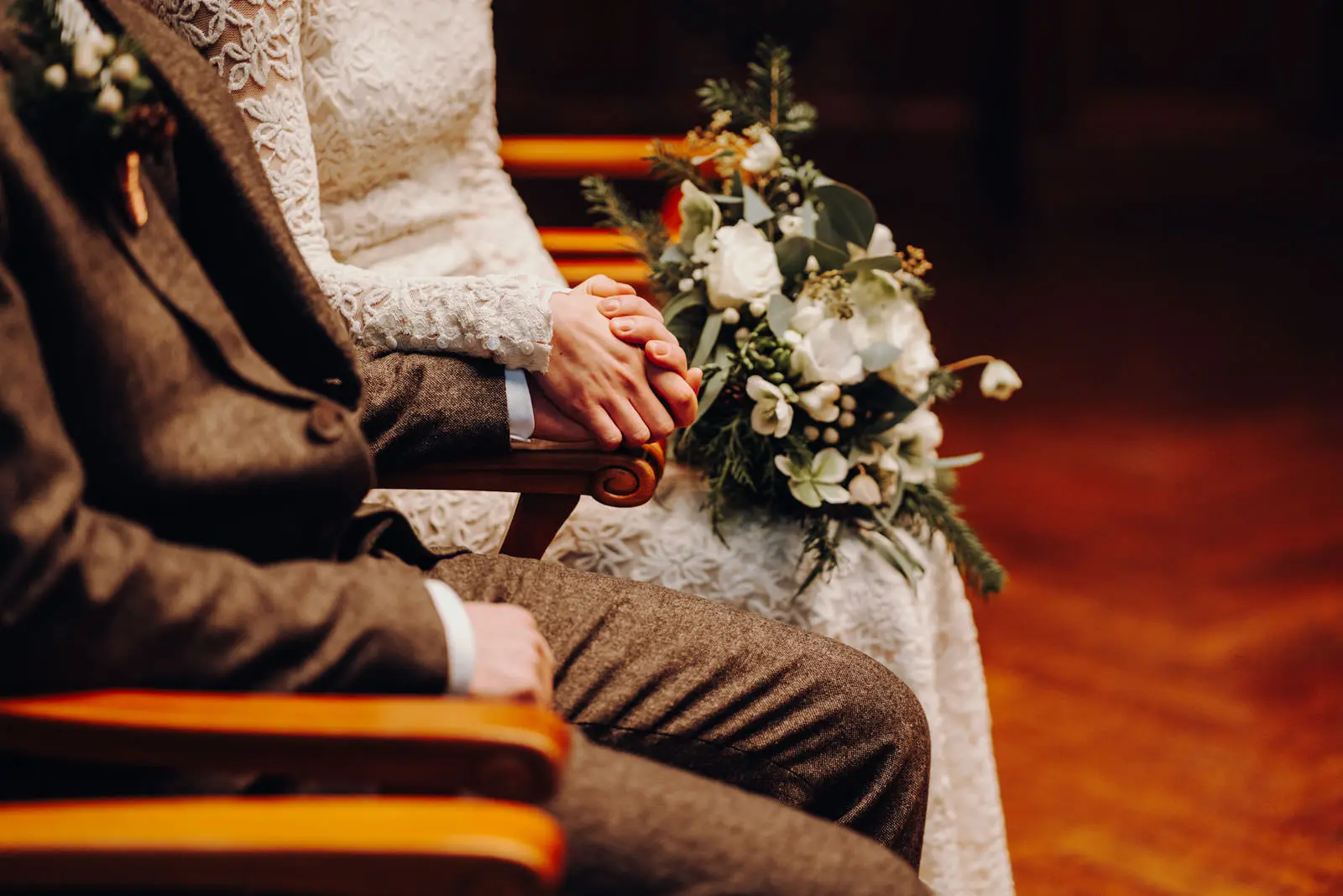 Haende halten waehrend der Trauung im Ratsplenarsaal Leipzig Brautpaar haelt sich an den Haenden waehrend der Hochzeit im Ratsplenarsaal Leipzig, Brautstrauss mit weissen Rosen und Eukalyptus im Vordergrund.