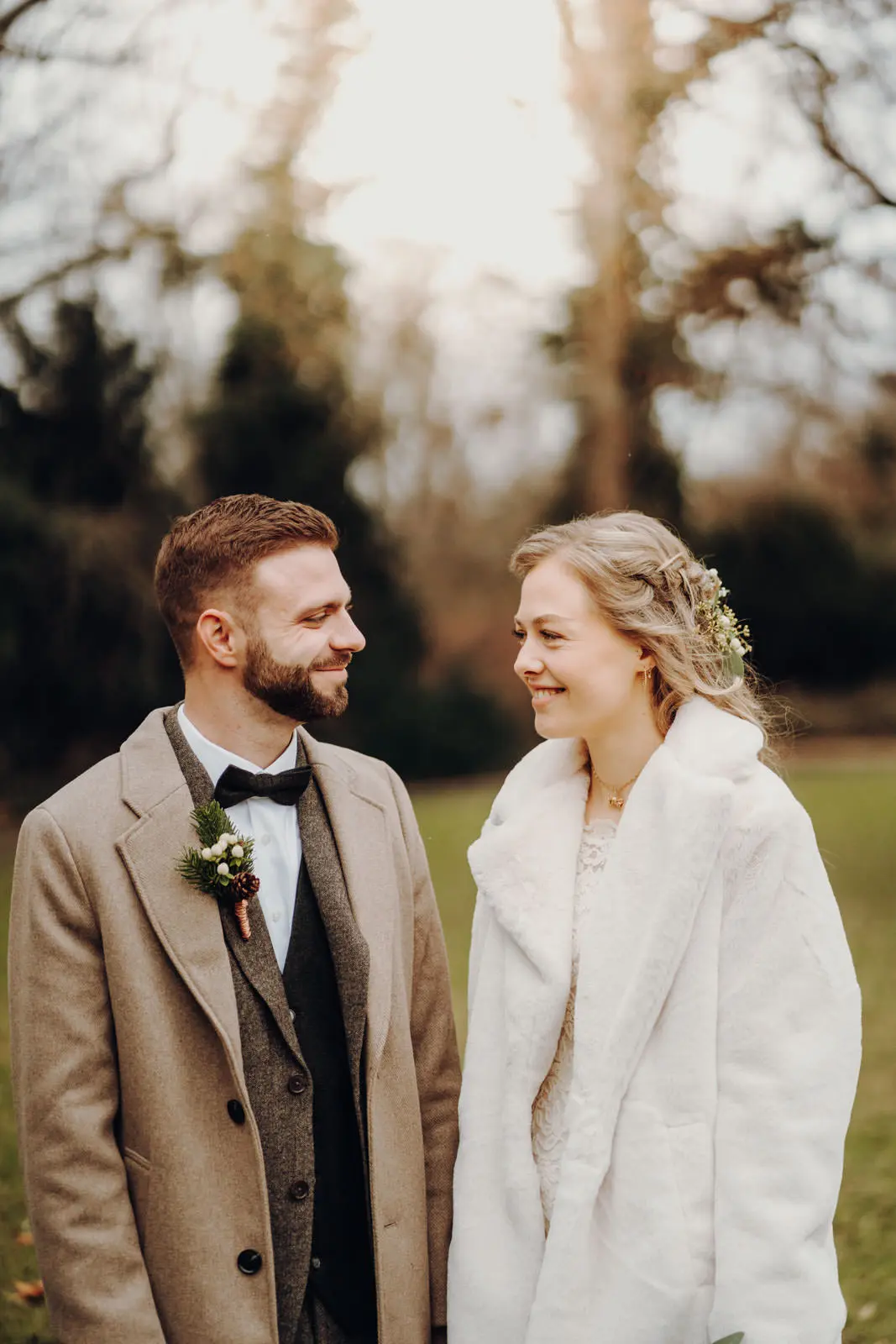 Brautpaar lacht sich an im Park nach der Hochzeit Braut und Braeutigam stehen sich gegenueber und laecheln sich herzlich an, Aufnahme im winterlichen Park nach der Trauung.