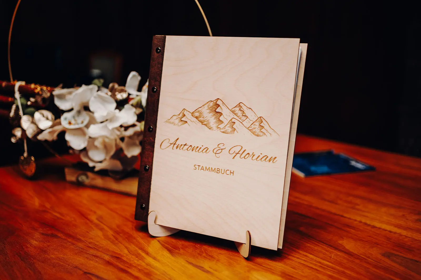 Stammbuch Antonia und Florian – Holzcover mit Berggravur Personalisiertes Stammbuch mit Holzcover, Berggravur und den Namen Antonia & Florian auf dem Trautisch.