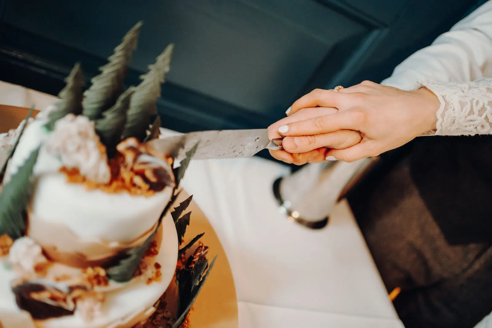 Haende beim Anschneiden der Hochzeitstorte Nahaufnahme der Haende des Brautpaares mit Messer beim Anschneiden der mehrstoeckigen Hochzeitstorte mit Tannenbaum-Figuren.